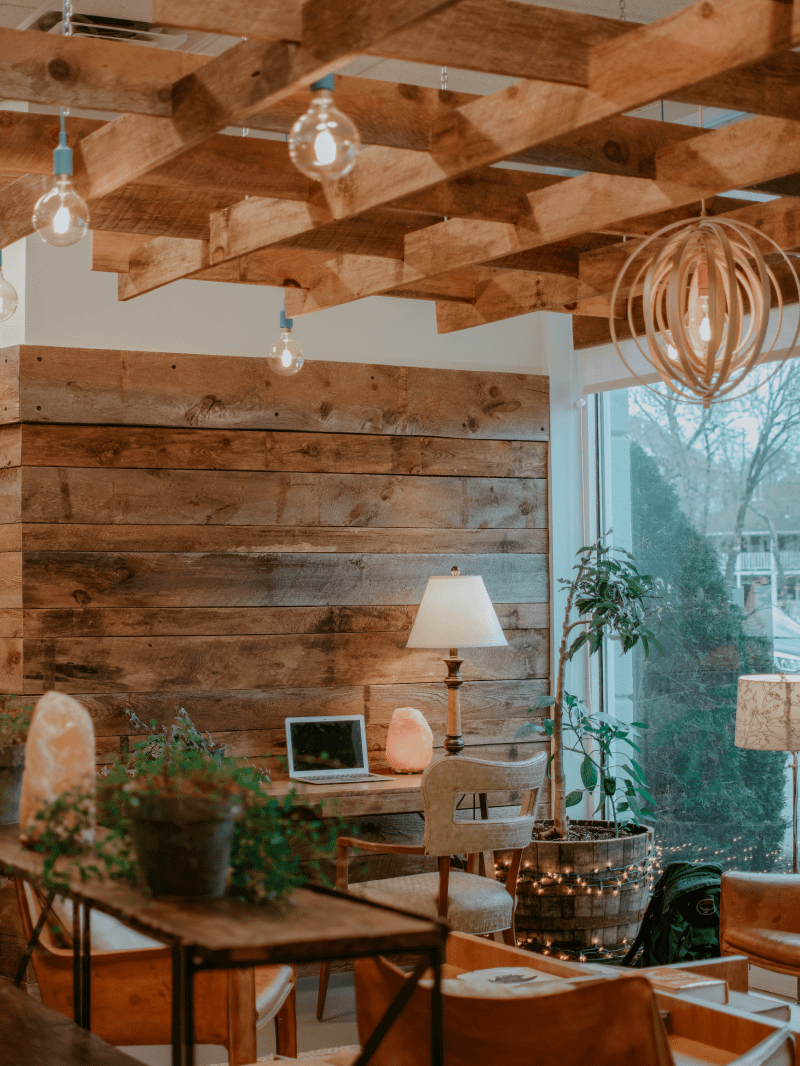 Wooden clad wall with a desk and laptop against it. Plants and fairy lights are around the desk