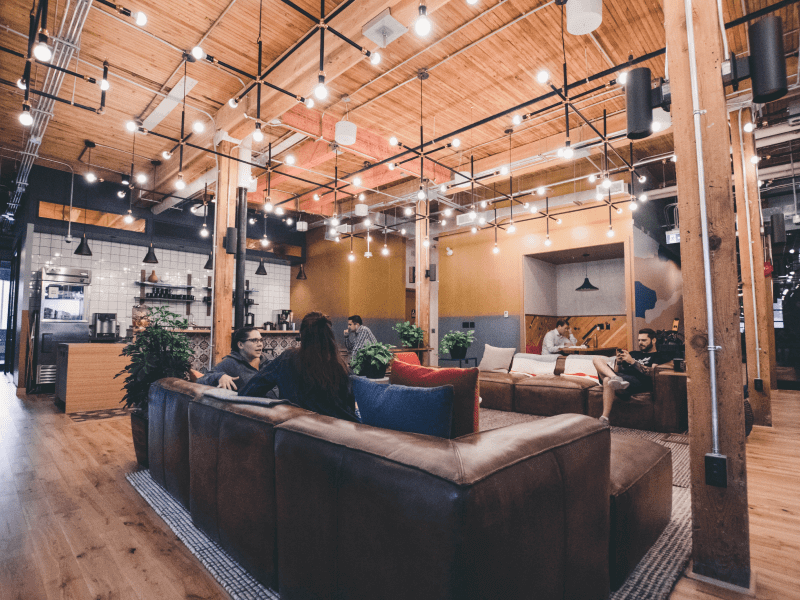 A cafe interior with brown leather sofas, looking up towards the wooden ceiling with hanging lightbulbs