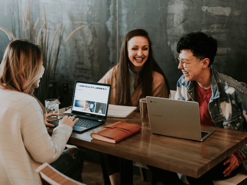 A group of three friends, laughing while working on their laptops