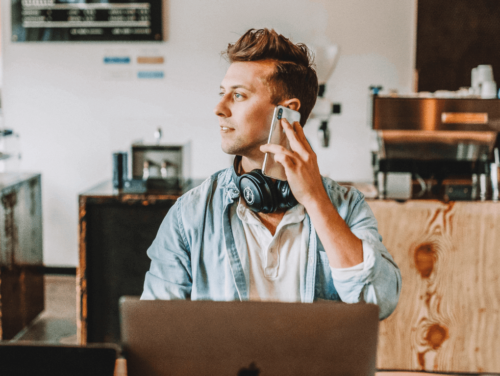 A man with a mobile against his ear, sitting in front of a laptop